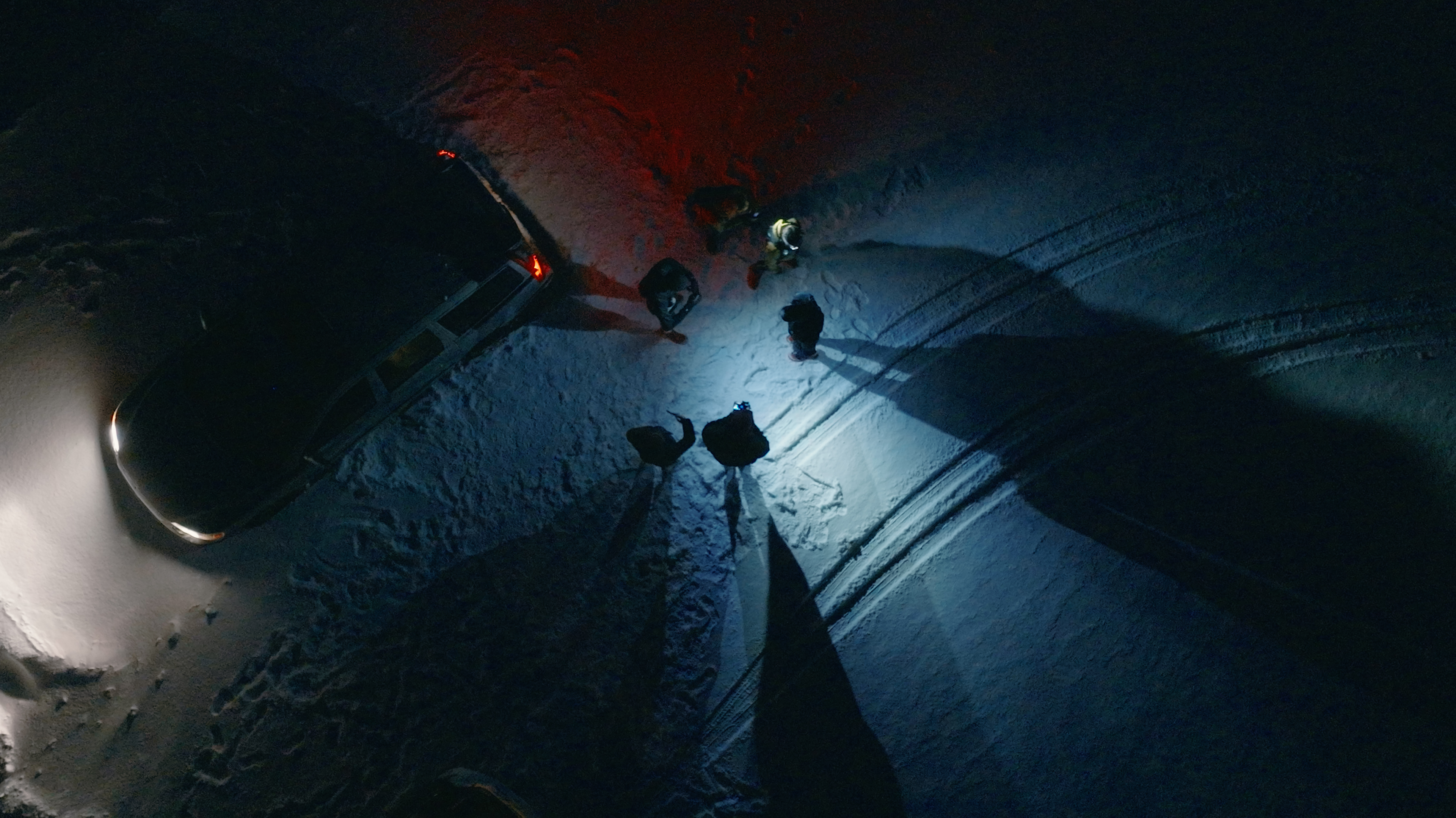 Overhead view of runners gathered at night in the snow by car headlights